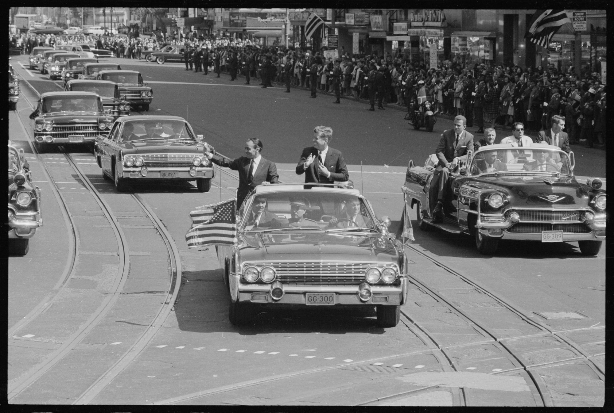 President Kennedy and King Hassan II of Morocco standing in the open presidential car during a welcoming parade in Washington, March 1963
