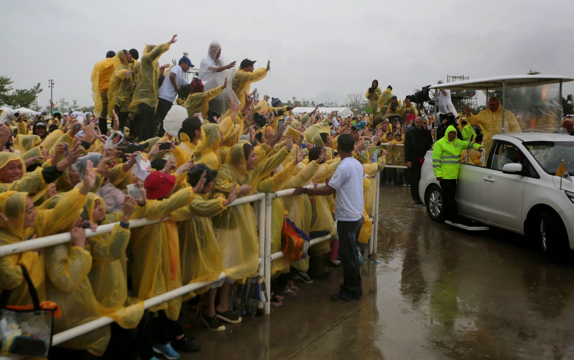 Papst Franziskus im gelben Regenmantel segnet aus einem offenen Papamobil bei Tacloban auf den Philippinen eine Menge in Regenjacken, Januar 2015
