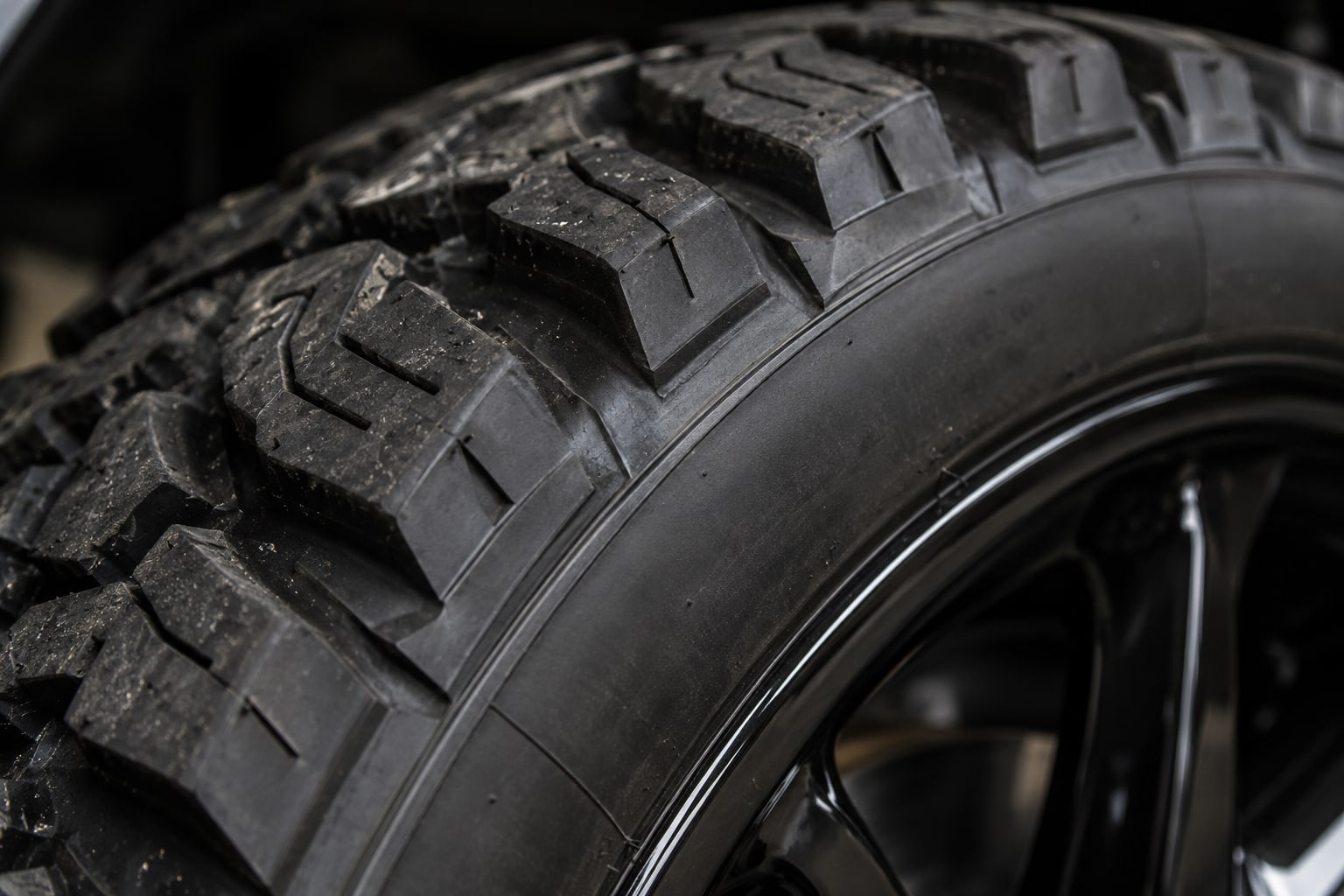 Extreme close-up of the tread and shoulder of a heavy-duty all-terrain tyre on a black wheel